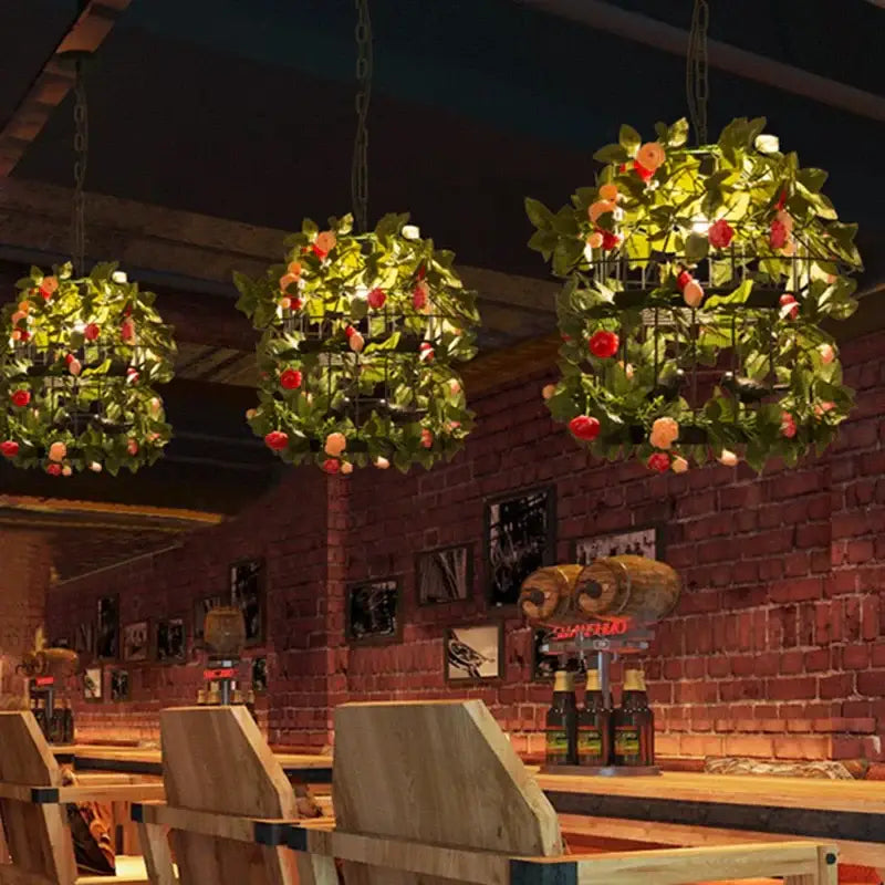 Industrial style rose chandelier with three black iron wireframe lights adorned with green leaves and red-orange flowers