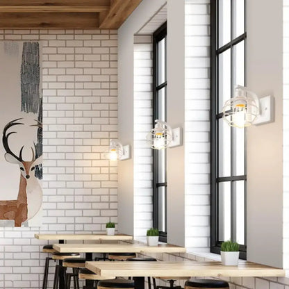 Industrial vintage black iron cage wall light with white metal cage and exposed bulb mounted beside tall windows