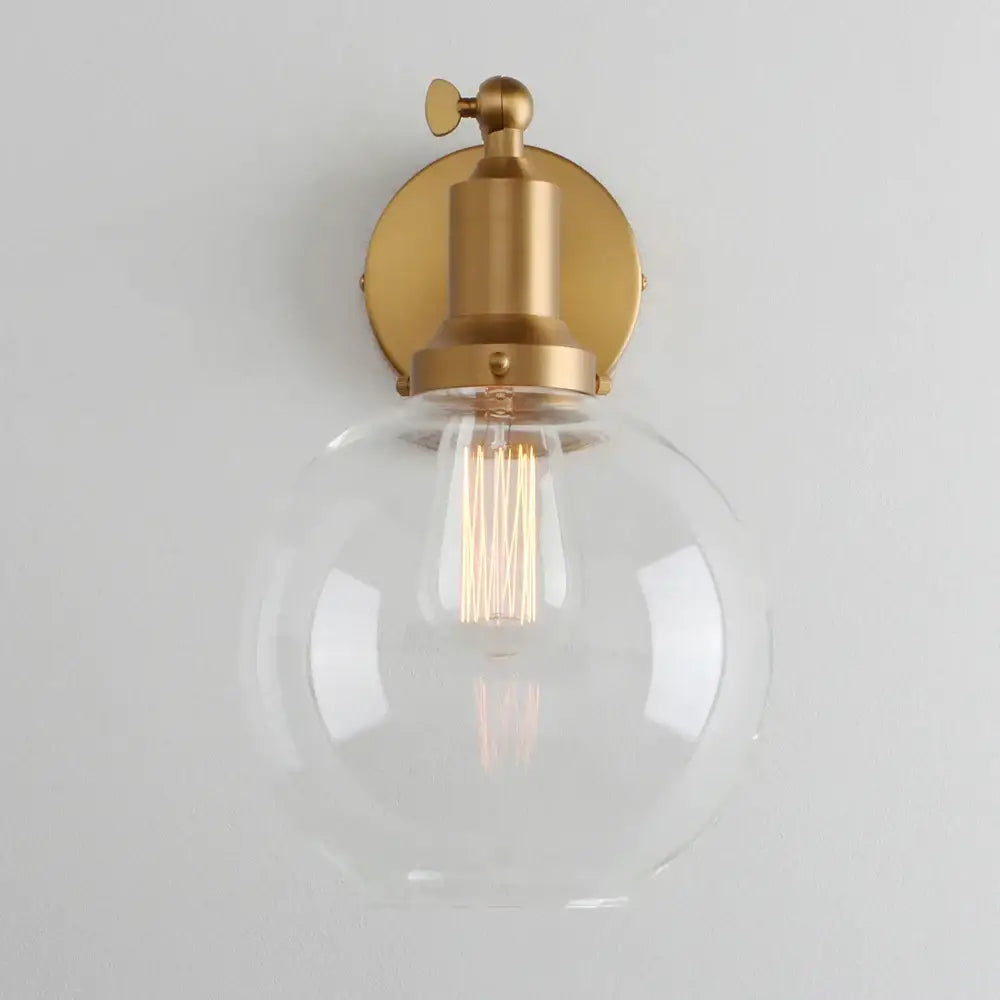 Industrial vintage wall sconce with a clear glass globe, brass-finished metal base, and exposed filament bulb for decorbites