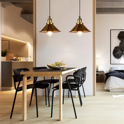 Two brass pendant lights with conical shades hang above a dining table in decorbites industrial vintage style