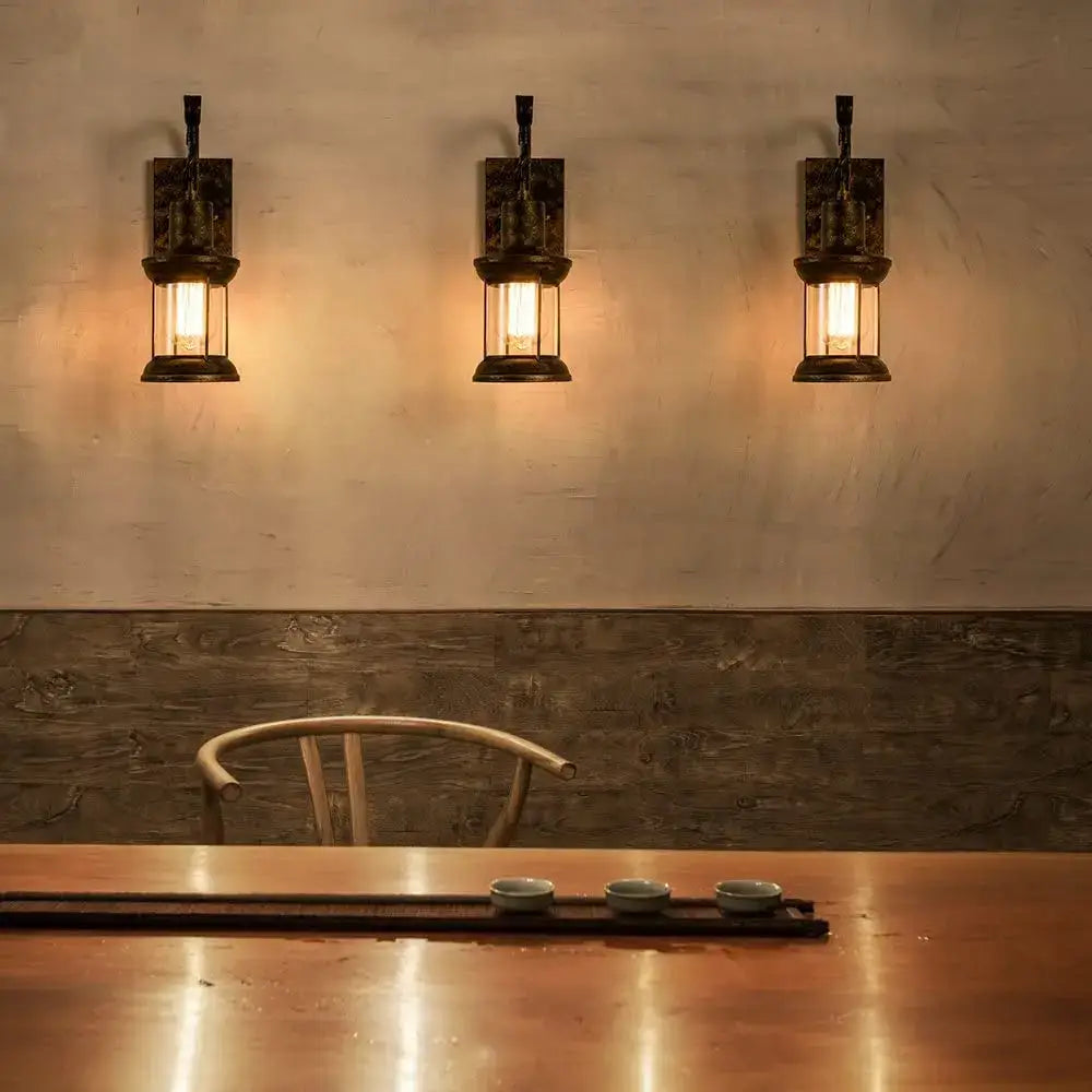 Three industrial vintage wall light sconces with antique bronze frames and glass lanterns emit warm golden light