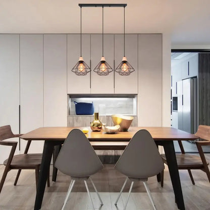 Three black metal cage pendant lights with warm bulbs hang above a wooden dining table in an industrial wood ceiling chandelier