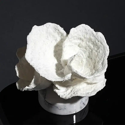 A sculpted white paper rose with layered petals on a marble base displayed alongside intricate pink glossy coral resin ornaments