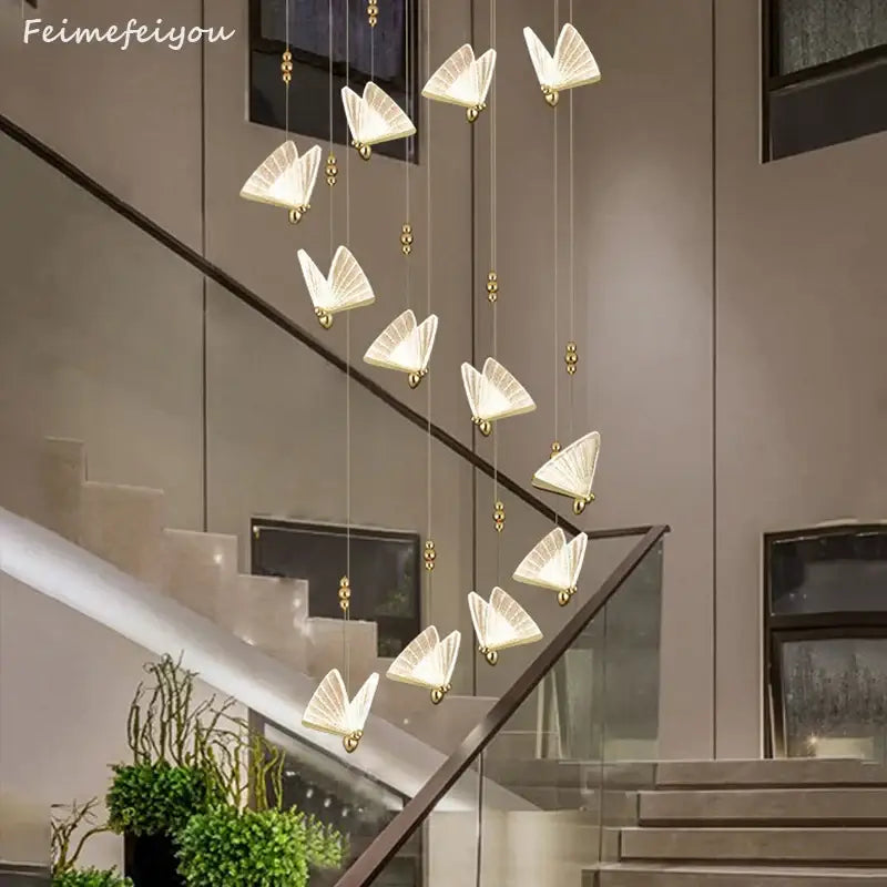 A modern iridescent gold butterfly pendant light with translucent white wings suspended above a staircase