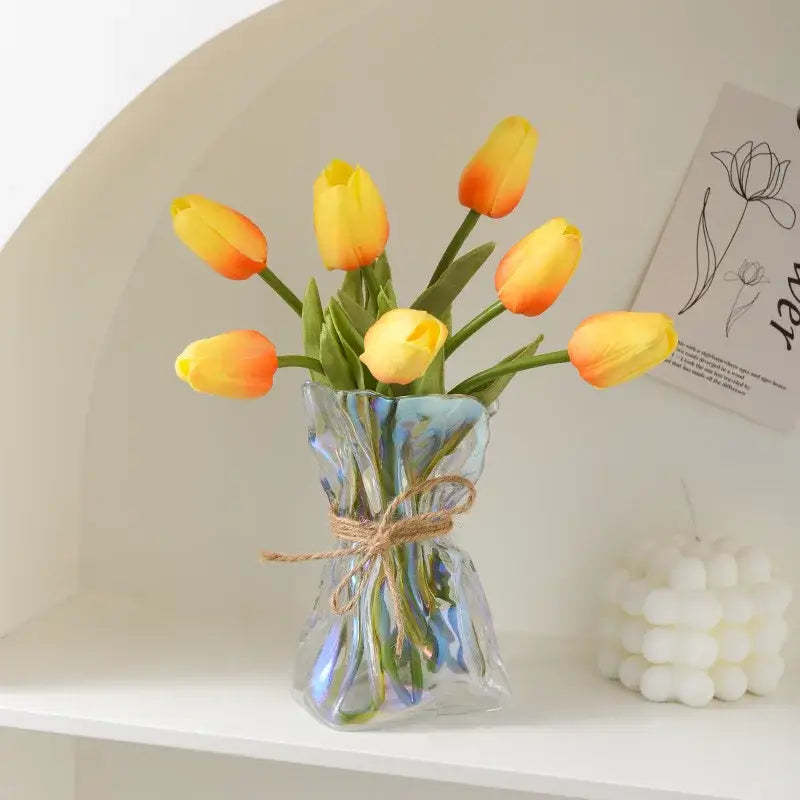 Irregular folded clear glass vase by decorbites with textured design and twine bow holding artificial yellow and orange tulips