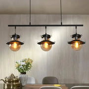 DecorBites 3-light linear island pendant with black metal frame and flared shade featuring amber globe shades