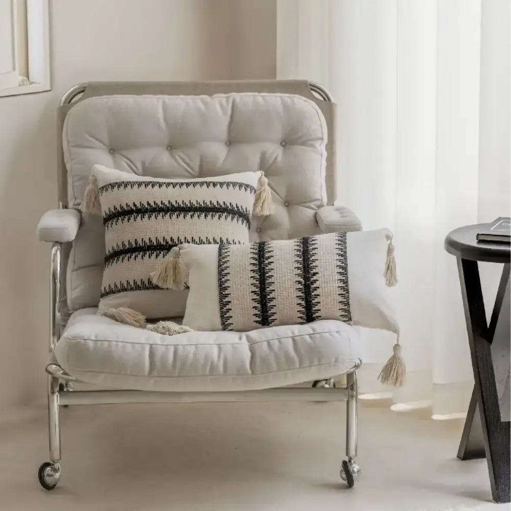 Beige tufted armchair with chrome frame and caster wheels featuring decorbites jacquard crochet pillow covers black and white tassels