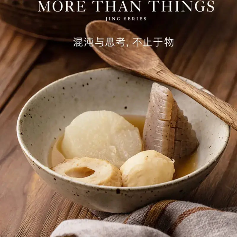 A hand made ceramic rice bowl set in beige and brown with speckled texture holding lotus root in light broth