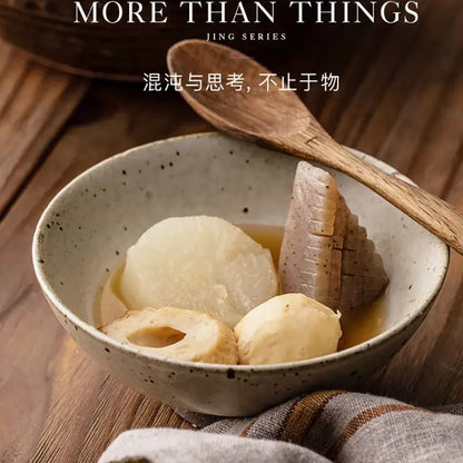 A hand made ceramic rice bowl set in beige and brown with speckled texture holding lotus root in light broth