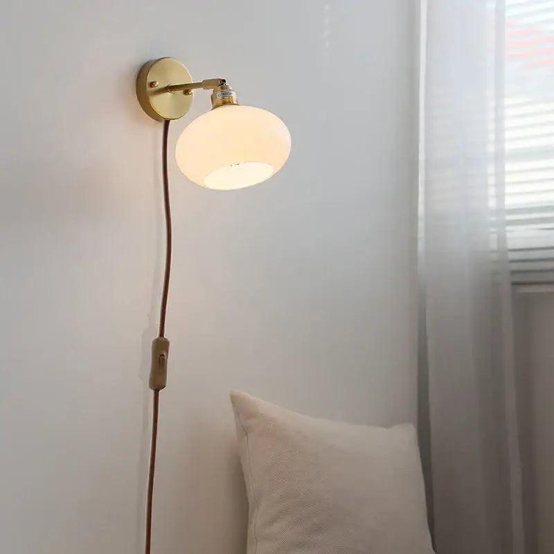A warm glowing japanese style led wall sconce with brass base and off-white frosted glass globe shade for bedroom decorbites