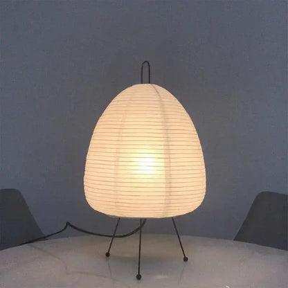 A warm glowing decorbites japanese style rice paper table lamp with a ribbed white shade and black metal legs for bedroom decor