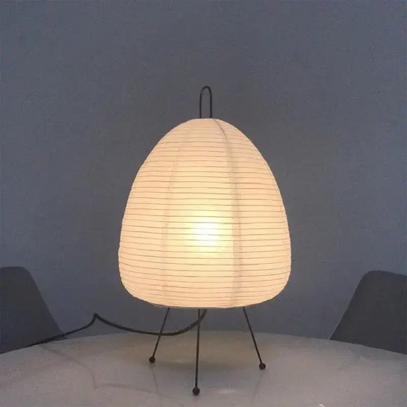 A warm glowing decorbites japanese style rice paper table lamp with a ribbed white shade and black metal legs for bedroom decor