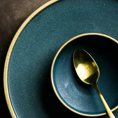 A matte teal decorbites ceramic dinner plate with gold rim paired with matching bowl and golden spoon for elegant dining