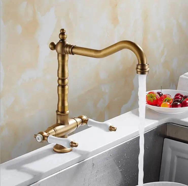 Antique brass single hole kitchen faucet with white ceramic handles and curved spout water flowing from nozzle