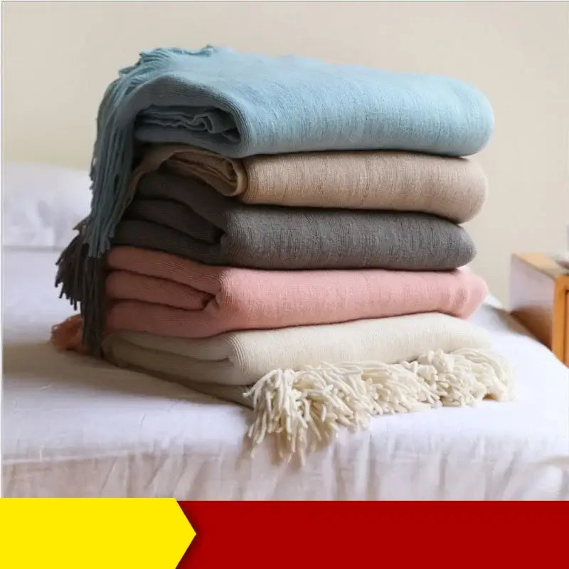 Stack of decorbites knitted cashmere siesta blankets in muted pastel tones with fringed edges for elegant bedroom decor