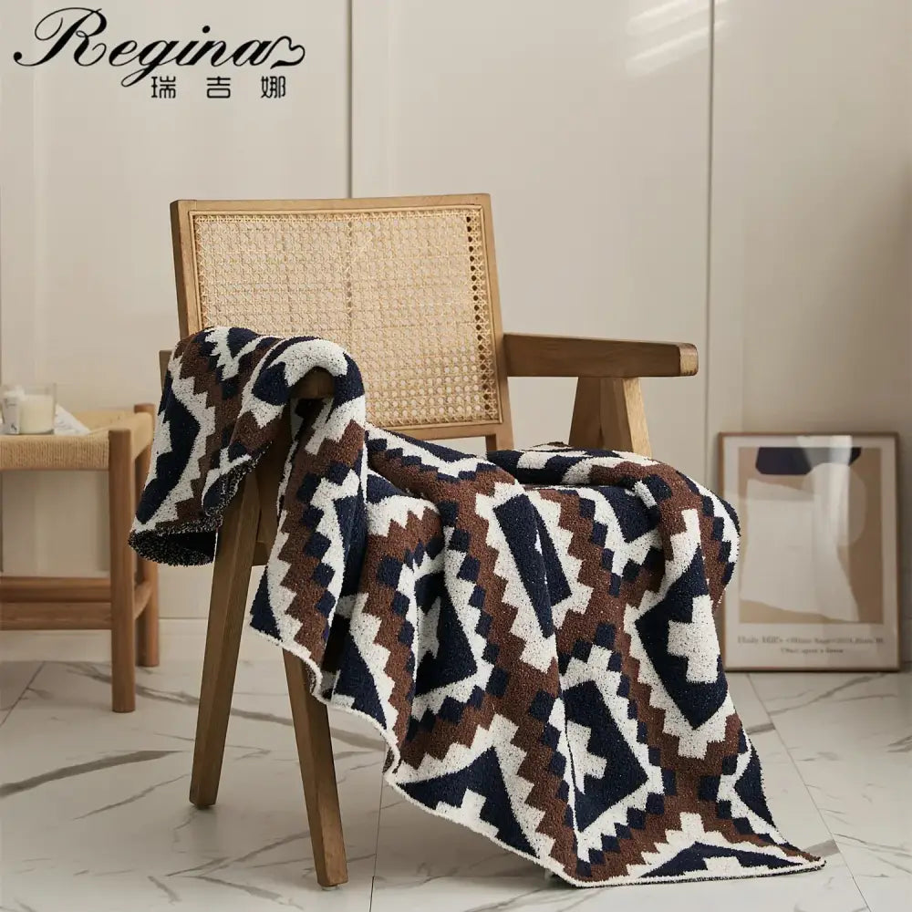 A decorbites knitted geometric quilt blanket in navy blue brown and white draped over a wooden chair