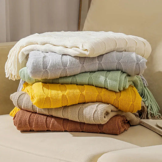 Stack of cozy decorbites knitted geometric throw blankets in soft pastel earthy tones with textured knit softness