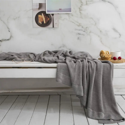 Gray knitted bamboo cooling throw blanket with textured weave and ribbed edges draped over white bench