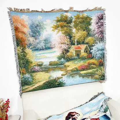 A decorbites jacquard sofa blanket featuring a woven pastoral scene with autumn trees and a cottage by a river