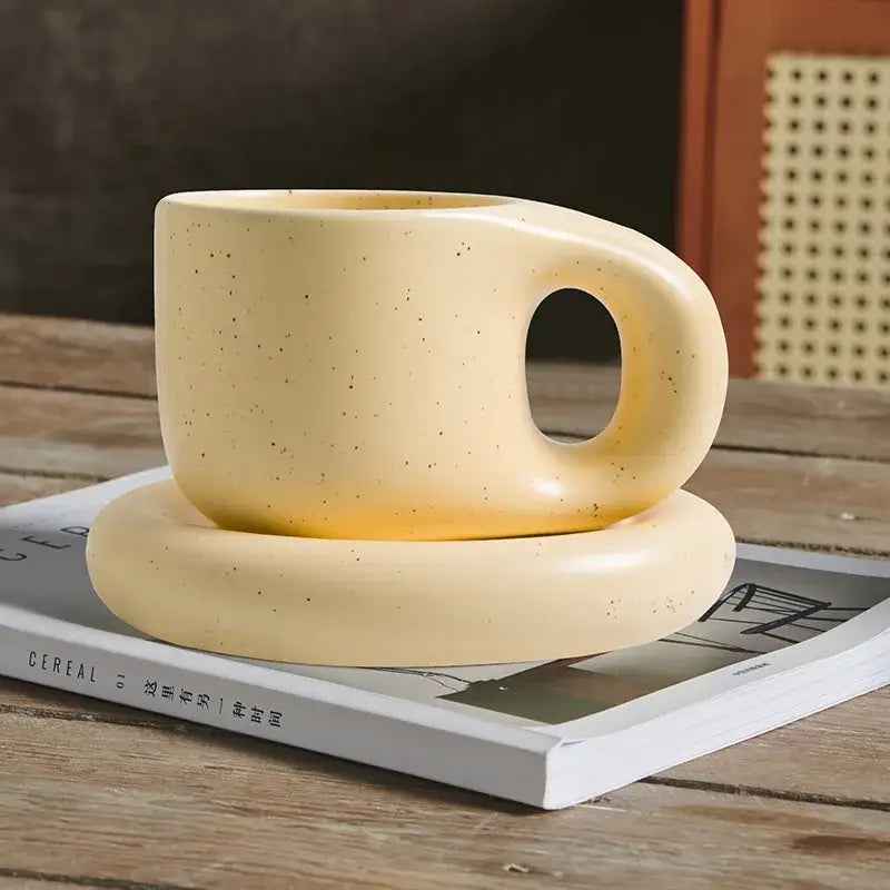 Cream-colored ink splash ceramic mug with speckled texture and rounded handle resting on matching oval plate decorbites ink splash set
