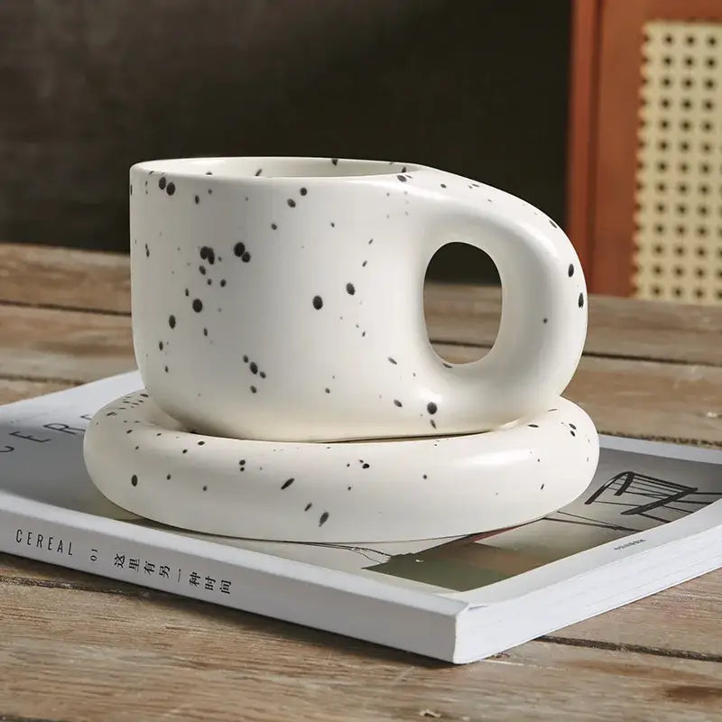 White ceramic ink splash mug with black speckles and rounded handle paired with decorbites ink splash oval plate