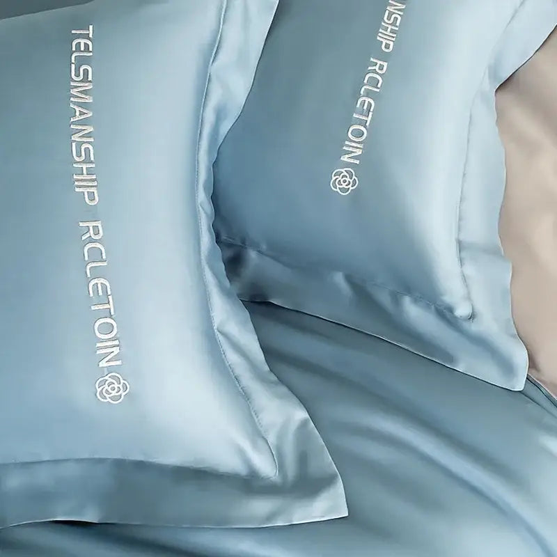 Light blue satin cotton embroidery pillowcases with white embroidered text and logo in a decorbites bedding set