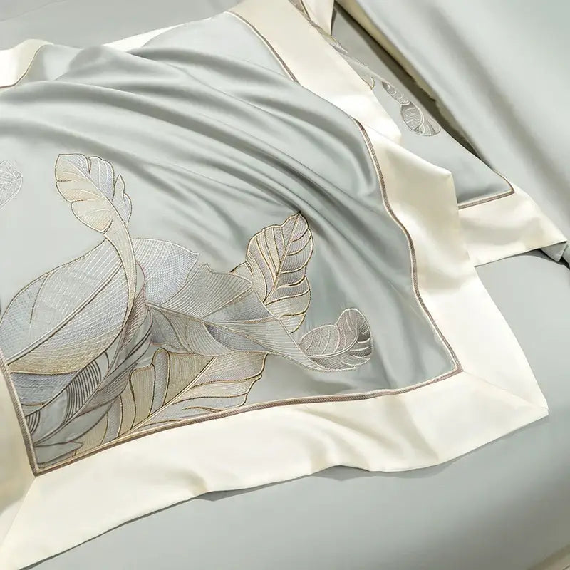 A light gray eucalyptus lyocell soft satin pillowcase with gold leaf embroidery and cream border in a bedding set