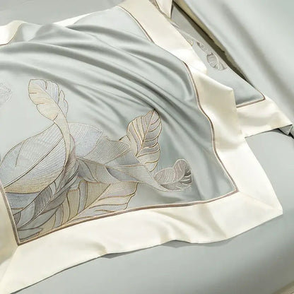 A light gray eucalyptus lyocell soft satin pillowcase with gold leaf embroidery and cream border in a bedding set
