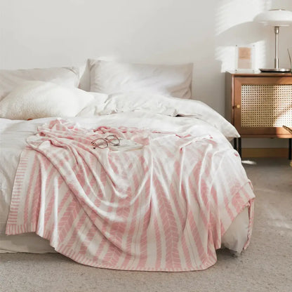 A soft pink and white striped bamboo knitted cooling blanket with light green leaf pattern draped over a bed decorbites cooling blanket