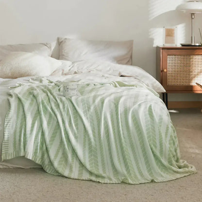 A soft mint green decorbites bamboo knitted cooling blanket with leaf pattern draped over a bed for bedroom use