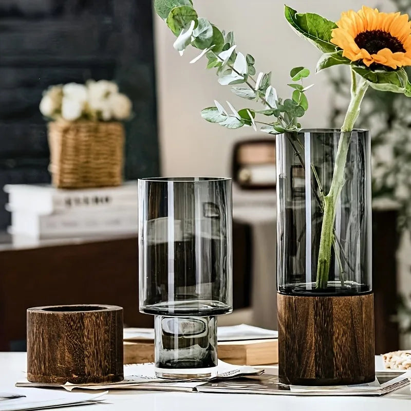 Tall translucent glass vase with dark wood base holding sunflower and eucalyptus for living room table decoration