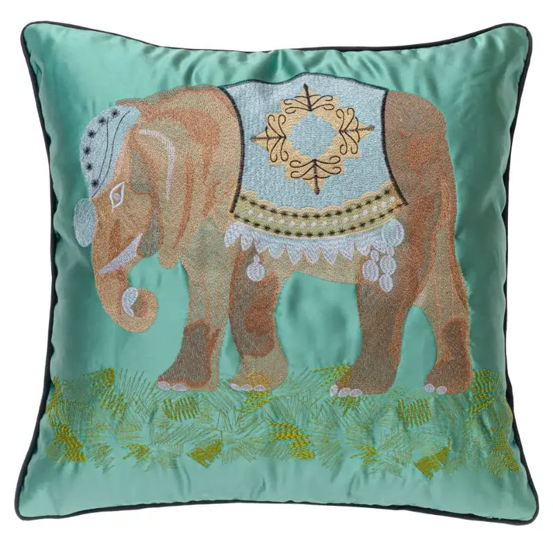 Teal satin cushion cover with decorbites elephant embroidery featuring a light blue and gold harness on green grass