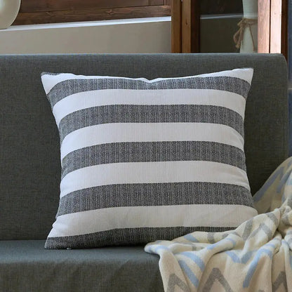 A linen stripe cushion cover with bold gray and white horizontal stripes on a dark gray couch from decorbites