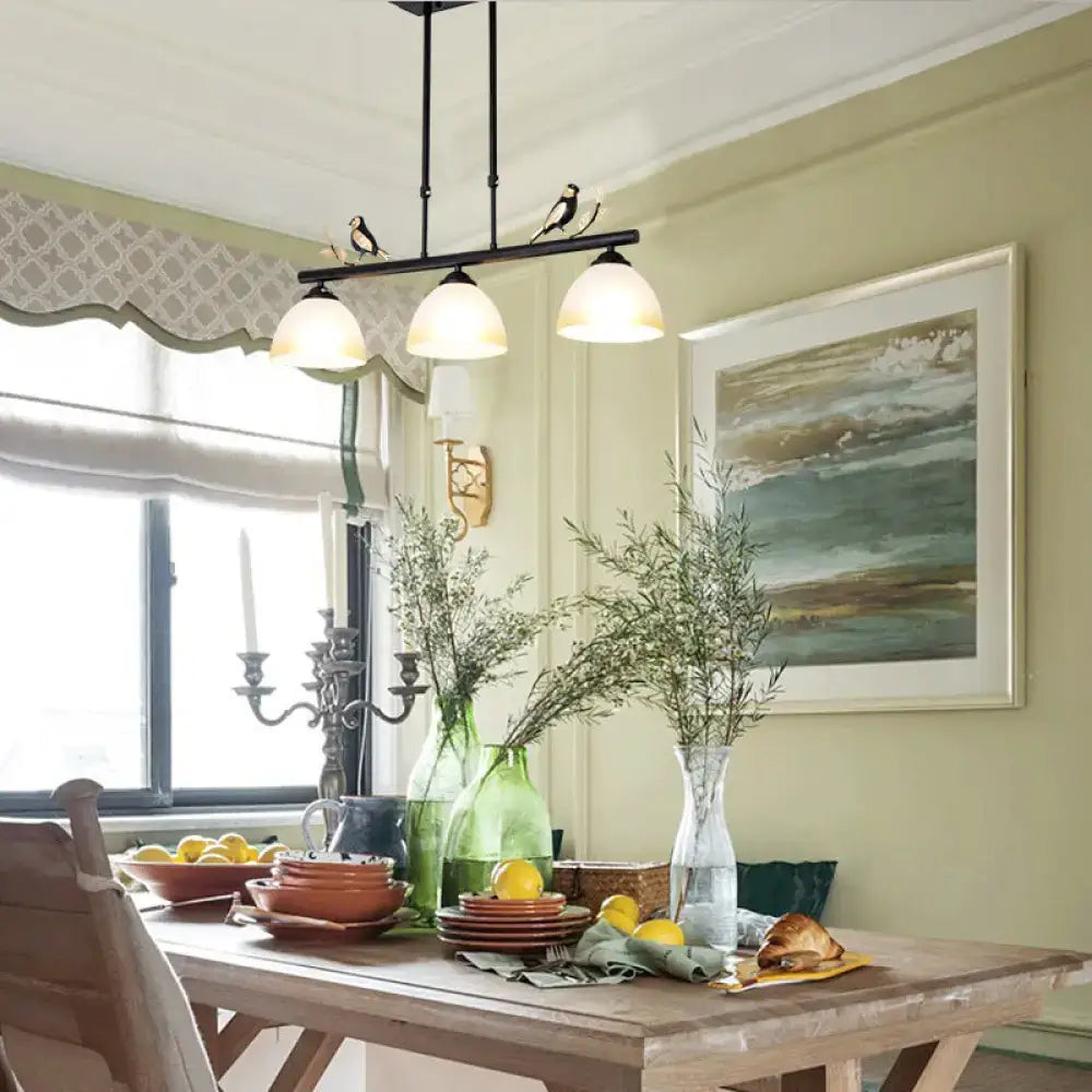 Black metal pendant light with three milky glass shades and decorative bird figures on black iron bar