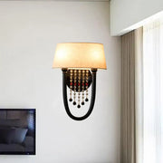 Black wrought iron wall lamp with beige fabric drum shade and crystal bead detail for bedroom decor