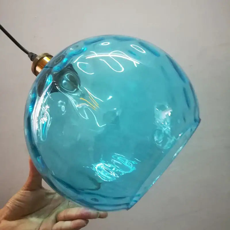 A translucent turquoise loft blue glass pendant light with a textured hand-blown surface and brass decorbites loft blue fixture