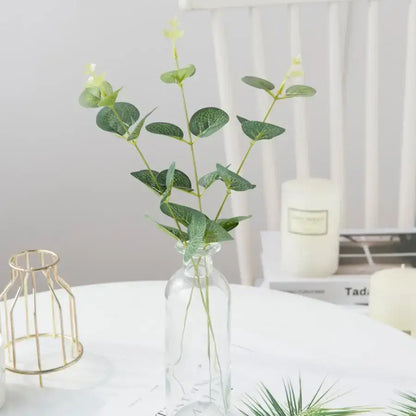 A clear glass vase holding artificial eucalyptus leaves with green foliage and yellow buds for decorbites eucalyptus leaves decor