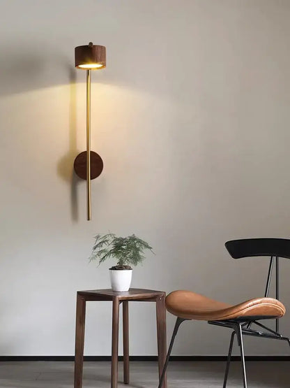 A luxury wall lamp with a brass stem and black walnut wood accents emitting warm light for bedroom reading