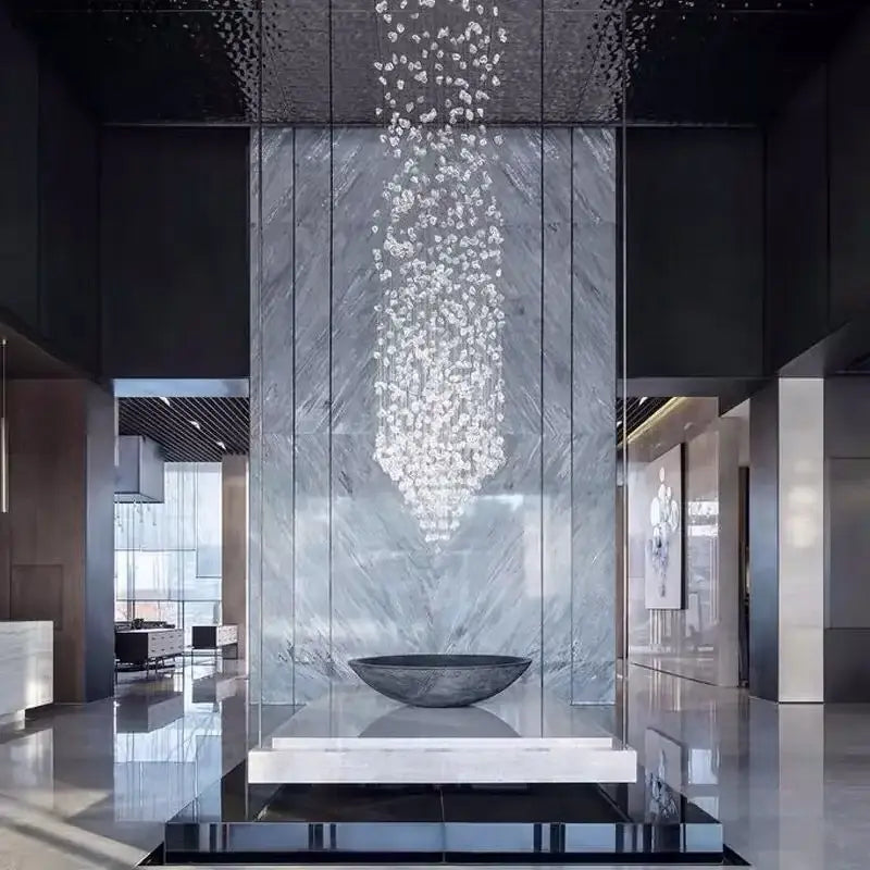Luxury cascading decorbites crystal led chandelier with clear faceted crystals above a dark gray stone bowl pedestal