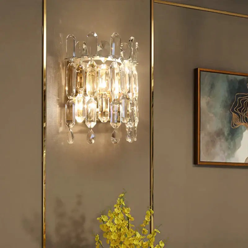 A luxury crystal wall lamp with gold-toned metal frame and cascading clear faceted glass prisms for elegant decorbites crystal wall lighting