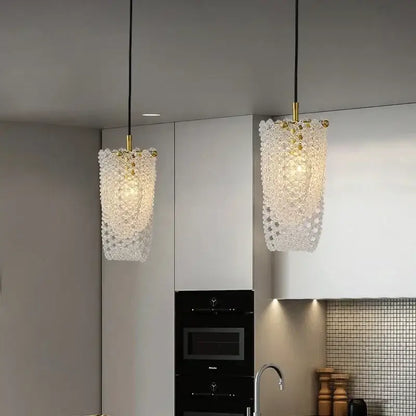 Two elegant gold crystal tassel pendant lamps with translucent crystal shades hang above a modern kitchen counter