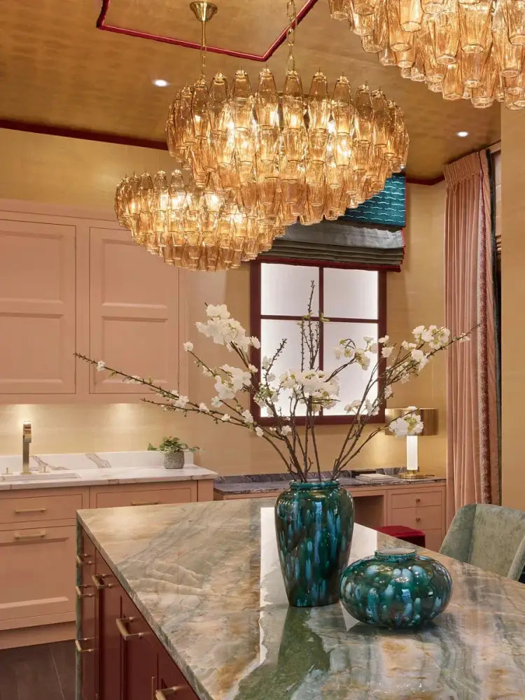 A tall glossy teal ceramic vase on marble countertop beside luxury decorbites gray glass chandelier with smoked crystal light fixture