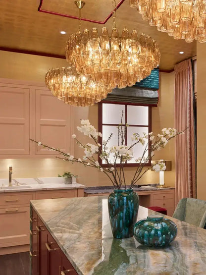 A tall glossy teal ceramic vase on marble countertop beside luxury decorbites gray glass chandelier with smoked crystal light fixture