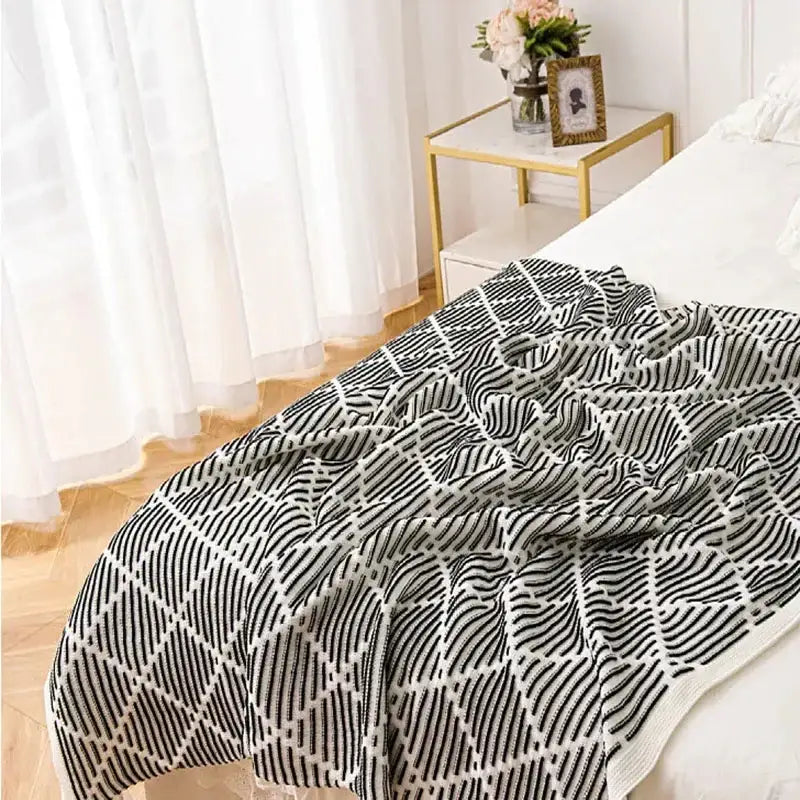A cozy black and white geometric-patterned decorbites knit sofa blanket with pom poms draped over a bed