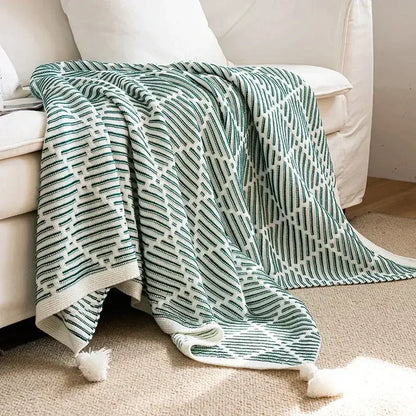 Luxury plaid decorbites knit sofa blanket in soft green and white with geometric pattern and fluffy pom pom tassels