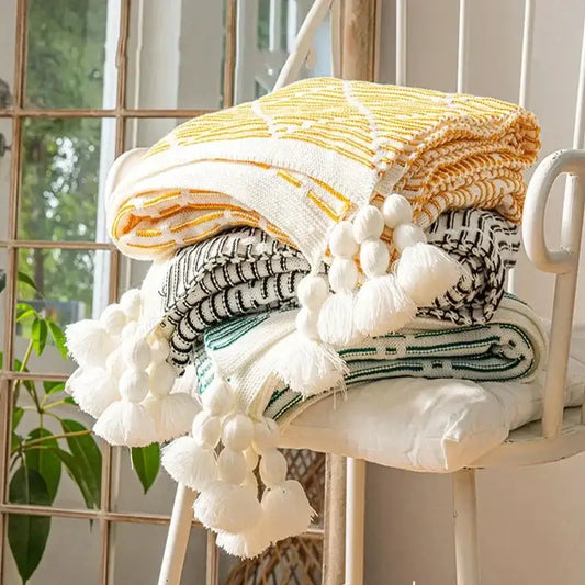 Stack of luxury decorbites knit sofa blankets in yellow black and white with fluffy pom-pom tassels for bedroom throw
