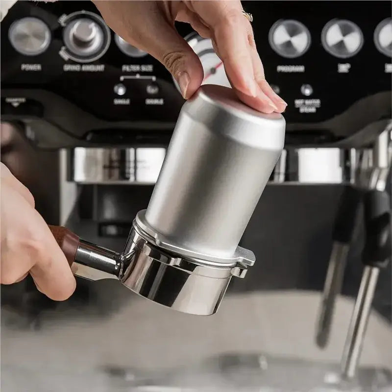 Silver metallic portafilter tamper with wooden handle used to tamp coffee grounds in front of matte black espresso dosing cup
