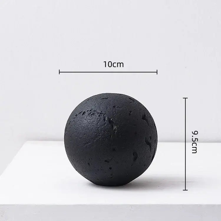 Matte black textured spherical home decoration accessory with rough surface and irregular indentations for living room