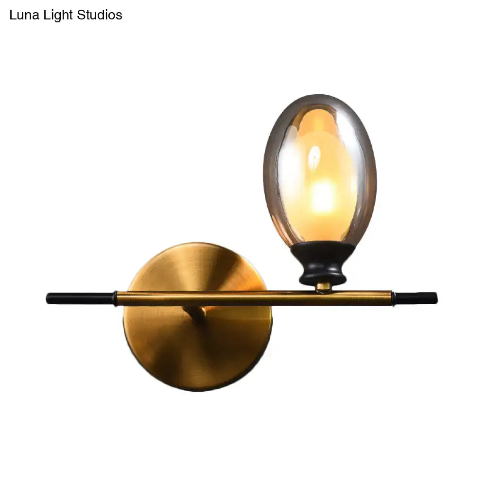 Mid century gold and black wall lamp featuring a gold-toned frame with a clear amber glass shade and black accents