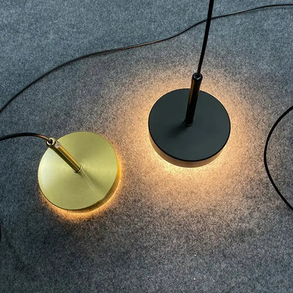 Two minimalist floor lamps with circular bases in brushed gold and matte black emit warm ambient glow near frosted white pendant light